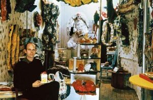 Artist Claes Oldenburg holding a cake sculpture at The Store.