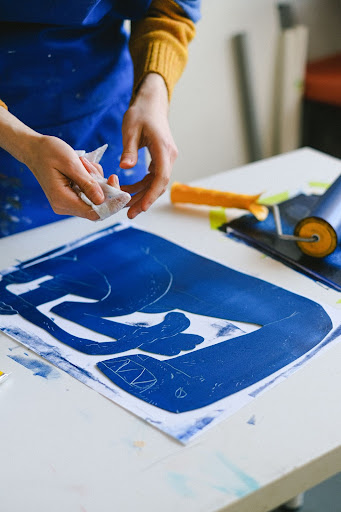 Artiste enlevant l'excès de répulsif acide de la plaque métallique avant d'appliquer l'acide.